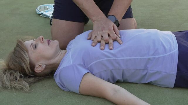 Paramedic performing cpr on unconscious woman on artificial turf