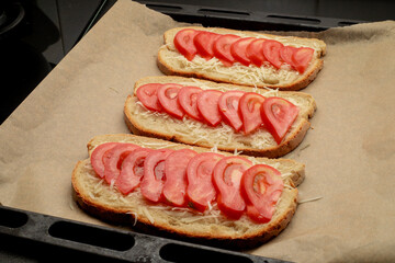 Close-up of tomato bruschetta on artisan bread slices with fresh sliced ​​tomatoes, parmesan cheese and herbs on a baking sheet in the oven while cooking. Food preparation process, bruschetta, sandwic