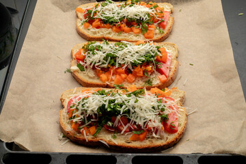 Close-up of tomato bruschetta on artisan bread slices with fresh sliced ​​tomatoes, parmesan cheese and herbs on a baking sheet in the oven while cooking. Food preparation process, bruschetta, sandwic