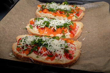 Close-up of tomato bruschetta on artisan bread slices with fresh sliced ​​tomatoes, parmesan cheese and herbs on a baking sheet in the oven while cooking. Food preparation process, bruschetta, sandwic