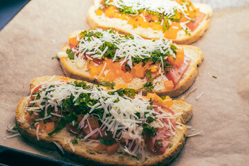 Close-up of tomato bruschetta on artisan bread slices with fresh sliced ​​tomatoes, parmesan cheese and herbs on a baking sheet in the oven while cooking. Food preparation process, bruschetta, sandwic