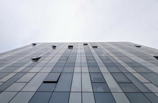 Ultra-wide low angle view of a modern glass office building with open windows and the bright sky in the background