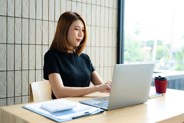 Asian businesswoman calculates finances on a clipboard with calculator by her laptop and smartphone...