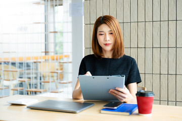 Asian businesswoman calculates finances on a clipboard with calculator by her laptop and smartphone...