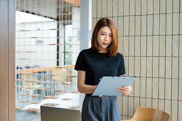 Asian businesswoman taps smartphone in a modern office workspace, highlighting digital...