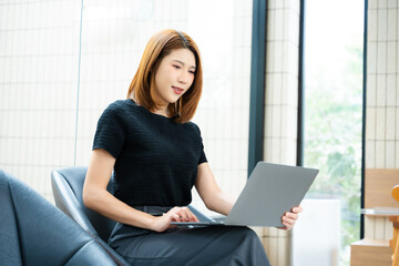 Asian businesswoman calculates finances on a clipboard with calculator by her laptop and smartphone in office