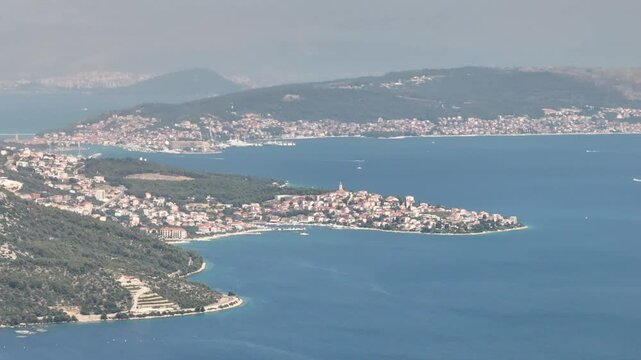 Aerial footage of Seget Vranjica, Croatia, with Trogir visible in the distance across the bay, highlighting coastal beauty and Mediterranean townscapes.