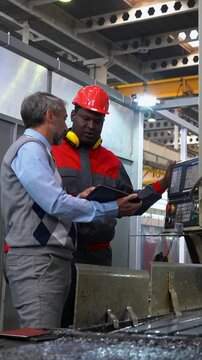 Production Manager Discussing about Job with Black CNC Machine Operator in a Factory. Middle-Aged Manager with Gray Hair, Using Digital Tablet in Communication with Young Worker. Industrial Leadership