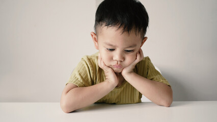 Little Asian boy sitting sadly with both hands supporting his chin on white background. Innocent boy