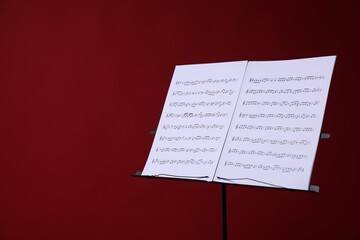 Note stand with music sheets on red background, space for text