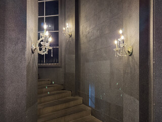 A dark, luxurious stairway illuminated by three ornate crystal wall sconces in an elegant building.