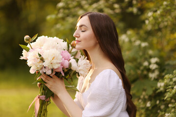 Beautiful woman with bouquet of peonies in park