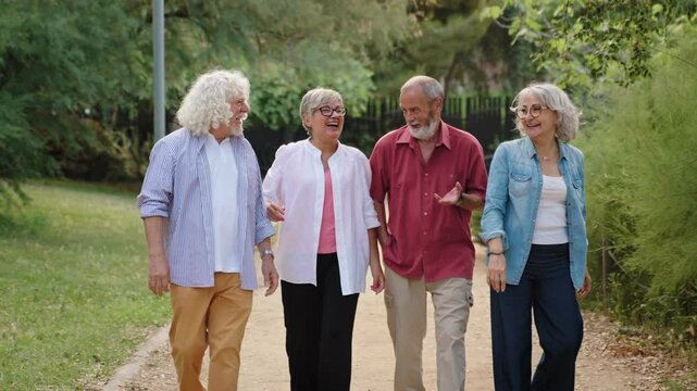 Group of four active healthy senior friends walking and having good times in public park, embracing and talking - Powered by Adobe