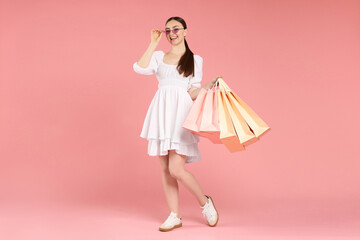Positive woman with shopping bags on light pink background