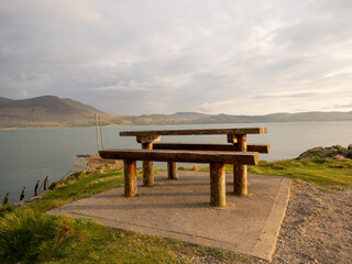 Wooden picnic table on a cliffside with panoramic views of mountains and the sea at sunset