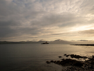 A calm sea reflects the soft golden light of dusk, with a solitary lighthouse on a distant islet