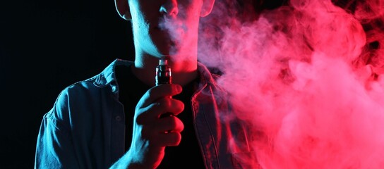 Man using electronic smoking device in neon lights on black background, closeup