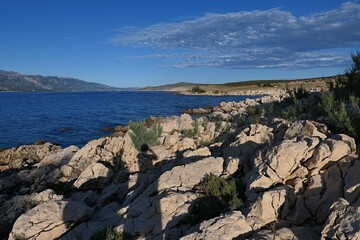 Summer landscape with rocky Croatian shoreline south of Razanac town, northern Dalmatia, Croatia. Bay water and arid foliage visible, blue skies in background. Late afternoon sunlight with shadows. 