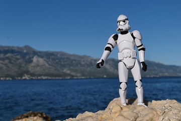 Naklejka premium Star Wars action figure of Clone Trooper in white armor and helmet standing on rocky beach of bay near Razanac, northern Dalmatia, Croatia, during july season. Velebit mountain in background, blue sky