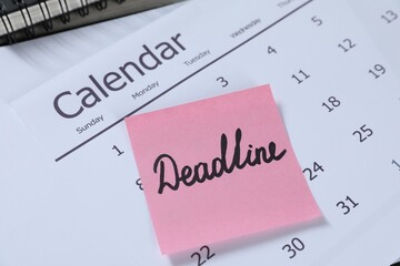 Sticky note with word Deadline and calendar on table, closeup