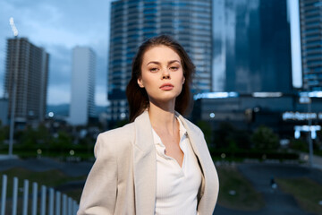 Confident woman with serious expression in business attire outdoors at twilight in urban financial...