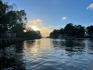Sunset Reflection Over Tranquil River With Lush Trees in the Background During Early Evening in a...