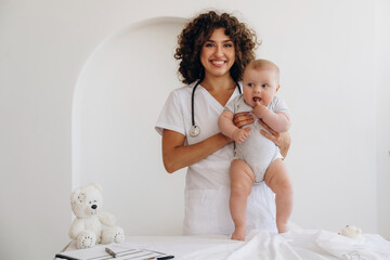 On the table and in hands, trying to stand up. Female doctor is with newborn baby indoors