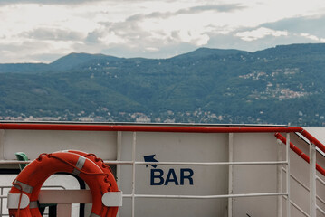 Ferry navigating Lake Maggiore, revealing alpine peaks beneath overcast skies, nautical safety equipment framing picturesque mountain panorama