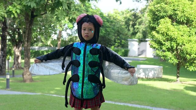 Young girl in a shiny bug costume with wings and antennae stands confidently in a green garden