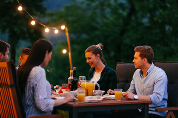 A group of young diverse people having dinner on the terrace of a modern house in the evening. Fun...