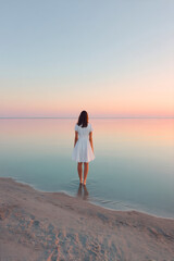 Woman in white dress stands at tranquil beach edge
