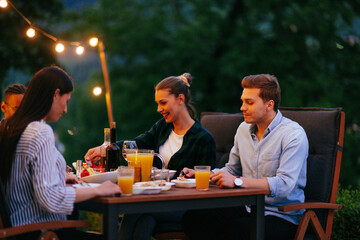 A group of young diverse people having dinner on the terrace of a modern house in the evening. Fun...