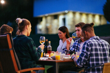 A group of young diverse people having dinner on the terrace of a modern house in the evening. Fun for friends and family. Celebration of holidays, weddings with barbecue