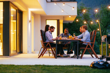 A group of young diverse people having dinner on the terrace of a modern house in the evening. Fun...