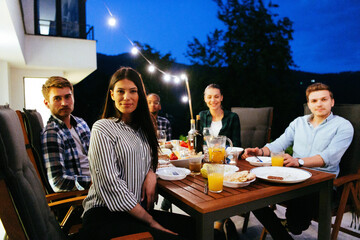 A group of young diverse people having dinner on the terrace of a modern house in the evening. Fun...