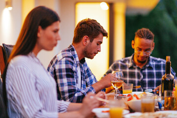 A group of young diverse people having dinner on the terrace of a modern house in the evening. Fun...