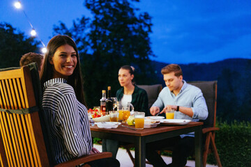 A group of young diverse people having dinner on the terrace of a modern house in the evening. Fun...