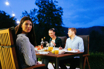 A group of young diverse people having dinner on the terrace of a modern house in the evening. Fun for friends and family. Celebration of holidays, weddings with barbecue