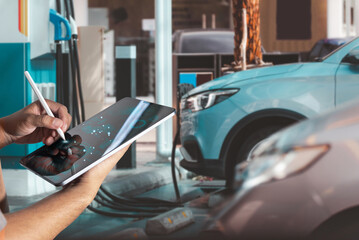 Technician using digital tablet for diagnostics and data analysis while an electric vehicle charges...