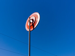 Large orange signal disc mounted on a pole against a clear blue sky during bright daylight,...