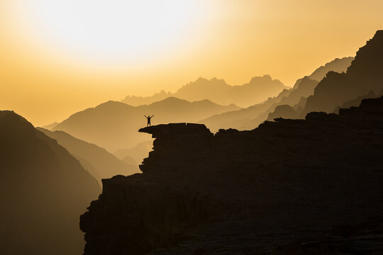 Sonnenuntergang &uuml;ber dem Al Shaq canyon, Ash Shaq Canyon in Saudi Arabien mit Person auf einem Felsen als Silhouette vor einer Berglandschaft im Abendlicht