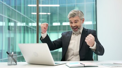 Happy excited businessman celebrates success after receiving great news on laptop sitting at workplace in business office. Shocked surprised smiling man in formal suit reads a positive good message