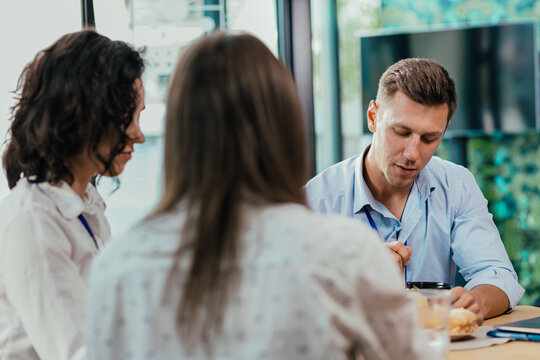 Young businessman eating healthy salad lunch with colleagues in modern office cafeteria - Powered by Adobe