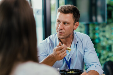 Young businessman eating healthy salad lunch with colleagues in modern office cafeteria