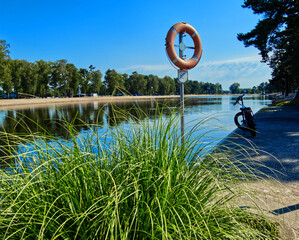 Electric bike resting beside lifebuoy on sandy lakeshore, pine trees framing sunny summer landscape