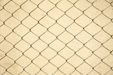 Close-up of a chain-link fence casting geometric shadows on a beige wall, creating a minimal...