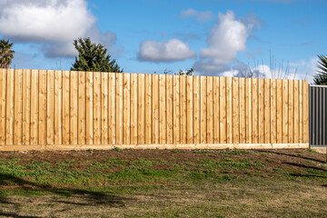 A newly installed vertical timber fence with neatly aligned wooden palings in a suburban backyard. a classic and modern boundary in Australian residential properties.