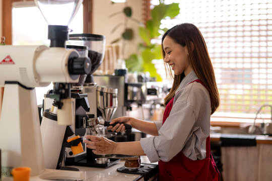 Smiling barista preparing coffee with professional grinder in cafe