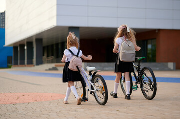 girls with bicycles arriving at school building. wearing uniforms and backpacks, they pause outside...