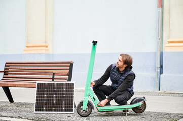 Man connects solar panel to electric scooter for charge, highlighting practical application of...